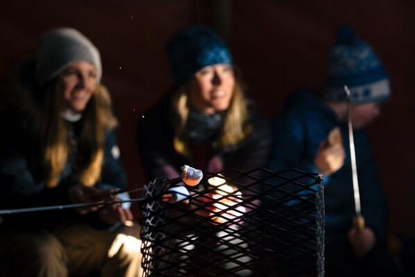 A group of people sitting around a campfire, with a metal grill in the foreground. - Fagernes Camping (Nord-Aurdal)