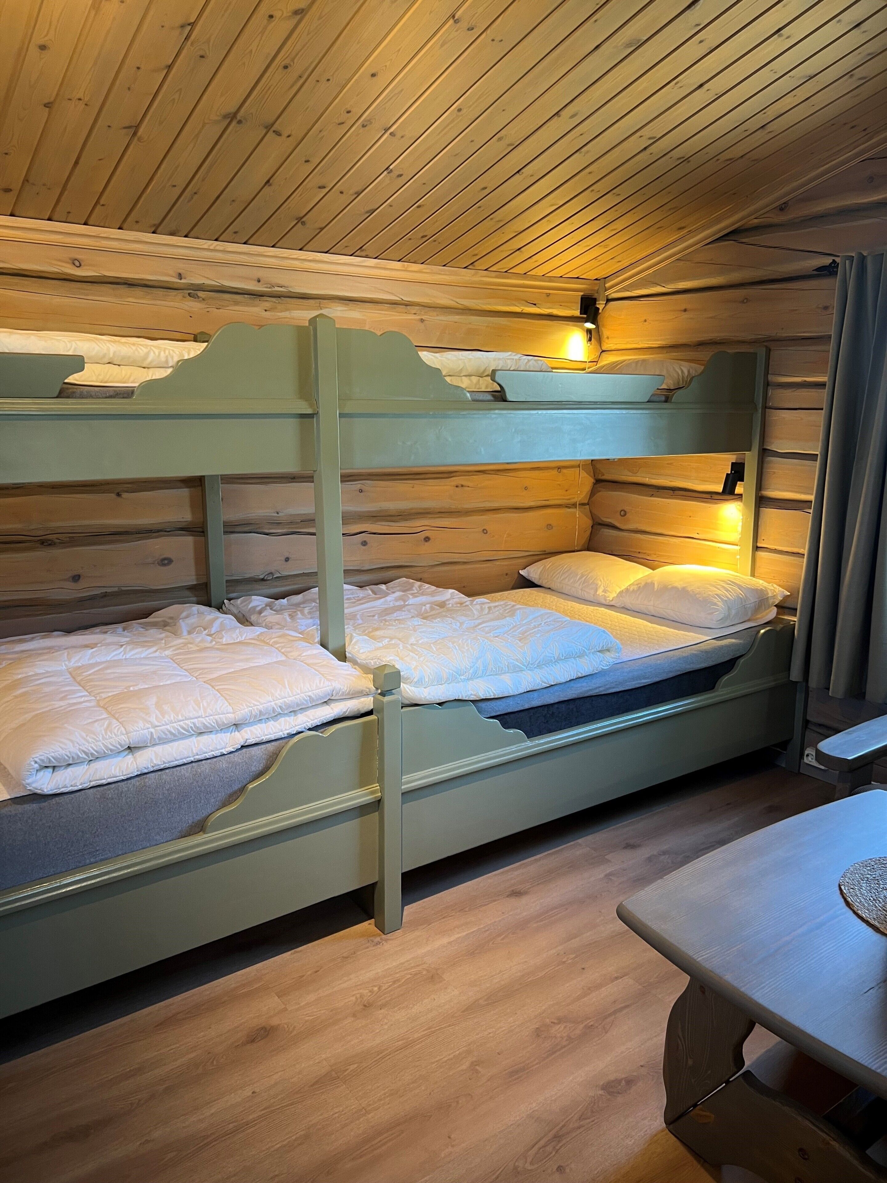 A bunk bed with two levels, a wooden ceiling, and a small table.