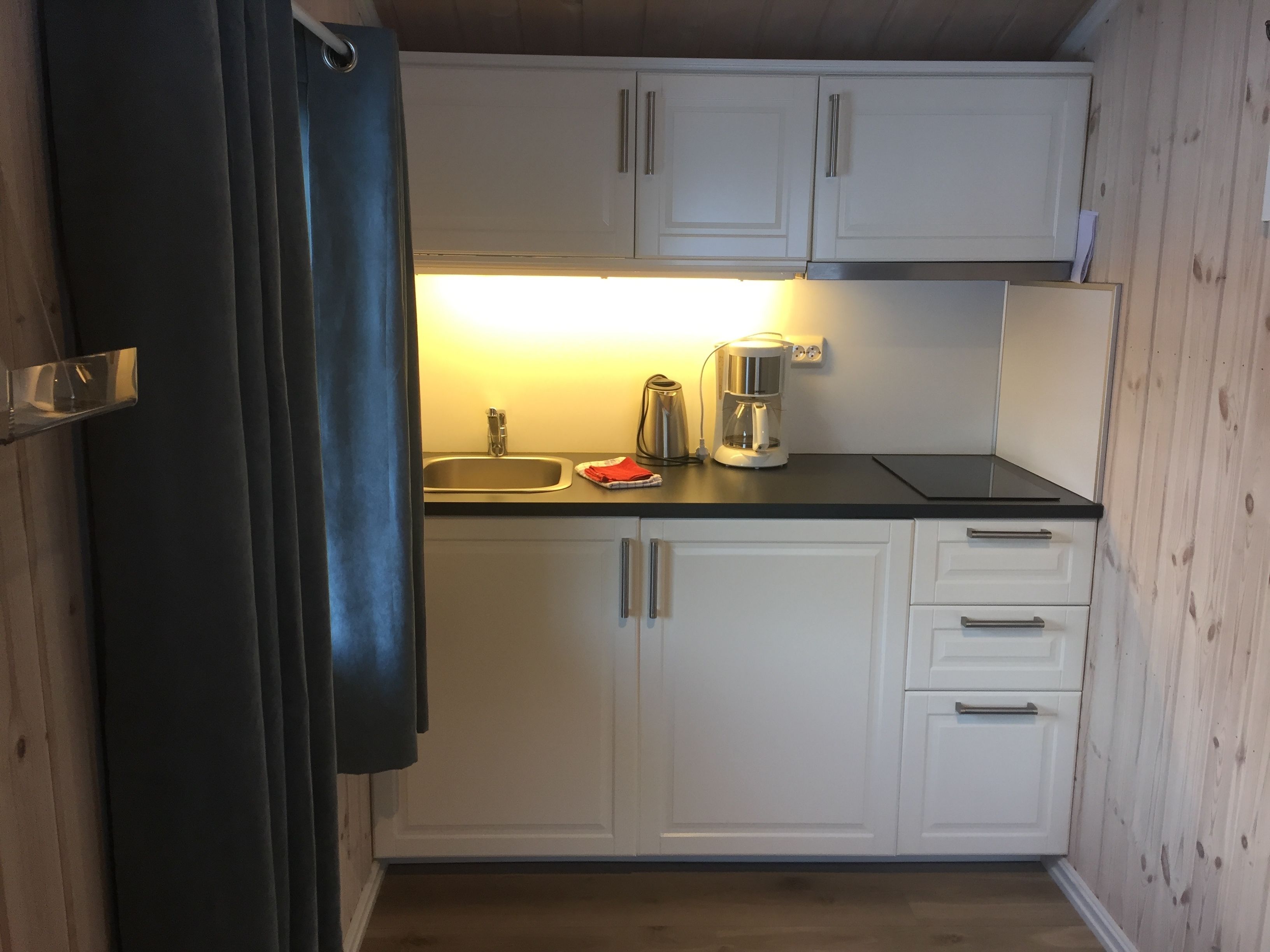 A compact kitchen with white cabinets, a black countertop, a stainless steel sink, and a coffee maker.