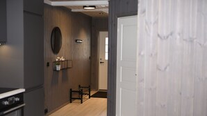 A modern kitchen with a built-in oven, a wooden wall with a circular mirror, and a bench with a small plant. - Fagernes Camping (Nord-Aurdal)
