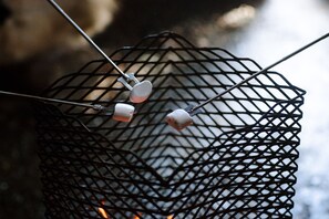 Una parrilla metálica con dos malvaviscos asándose sobre una llama abierta.