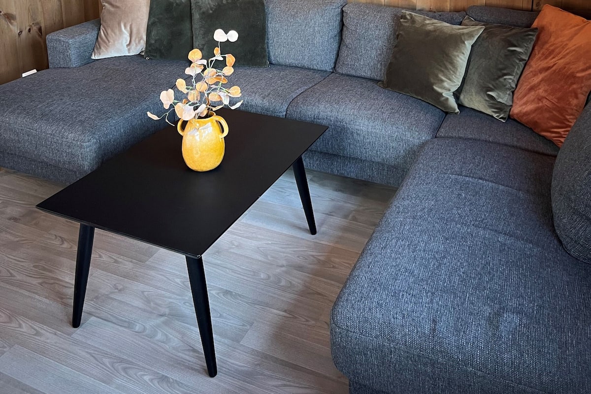 A modern living room with a sectional sofa, a black coffee table with a yellow vase, and a large deer painting on the wall.