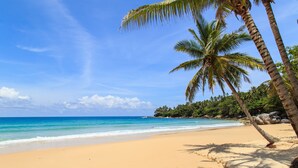 A beach with clear blue water, sandy shore, and palm trees. - Beautiful 3-Bedroom Villa at Surin Beach (Choeng Thale)