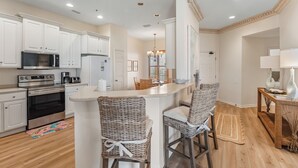 A modern kitchen with white cabinetry, stainless steel appliances, and a central island with bar stools. - 303W ~ Captivating 3BR/3BA condo with a Gulf view (Gulf Shores)