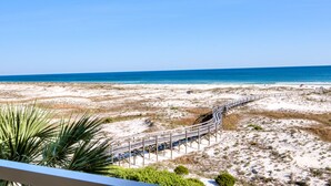A beach view with a wooden boardwalk leading to the water, surrounded by sand dunes and sparse vegetation. - 303W ~ Captivating 3BR/3BA condo with a Gulf view (Gulf Shores)