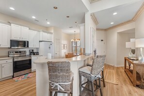 A modern kitchen with white cabinetry, stainless steel appliances, and a central island with bar stools. - 303W ~ Captivating 3BR/3BA condo with a Gulf view (Gulf Shores)