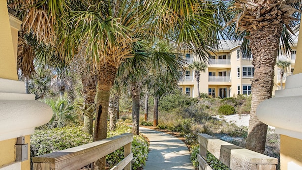 A wooden pathway leading to a building with balconies, surrounded by palm trees and greenery. - 303W ~ Captivating 3BR/3BA condo with a Gulf view (Gulf Shores)