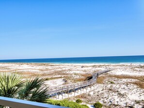 A beach view with a wooden boardwalk leading to the water, surrounded by sand dunes and sparse vegetation. - 303W ~ Captivating 3BR/3BA condo with a Gulf view (Gulf Shores)