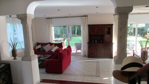 A spacious living area with a red sofa, a wooden cabinet, and a view of the garden through large sliding doors. - Casa da Agra, villa with pool and splendid garden (A Coruña)