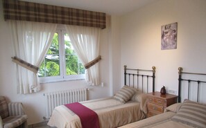 A bedroom with two beds, a radiator, a window with curtains, a chair, and a bedside table. - Casa da Agra, villa with pool and splendid garden (A Coruña)