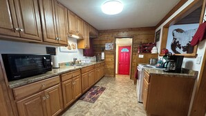 Una cocina con armarios de madera, un microondas, una puerta roja y una cafetera.