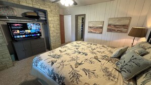 Un dormitorio con una cama grande, un televisor sobre un mueble y un ventilador de techo.