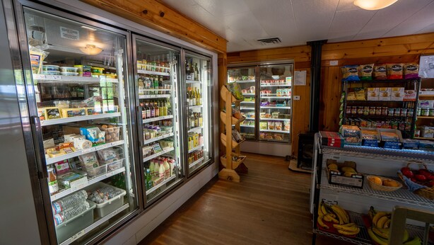 Interior de un supermercado con secciones refrigeradas, estantes llenos de diversos productos y un diseño de madera.
