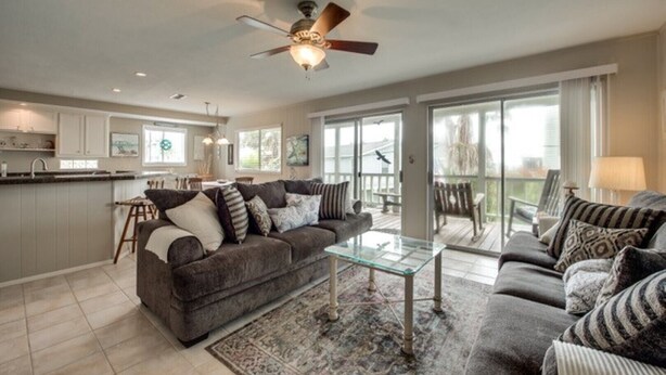 A spacious living room with a large gray sofa, a glass coffee table, and a ceiling fan.