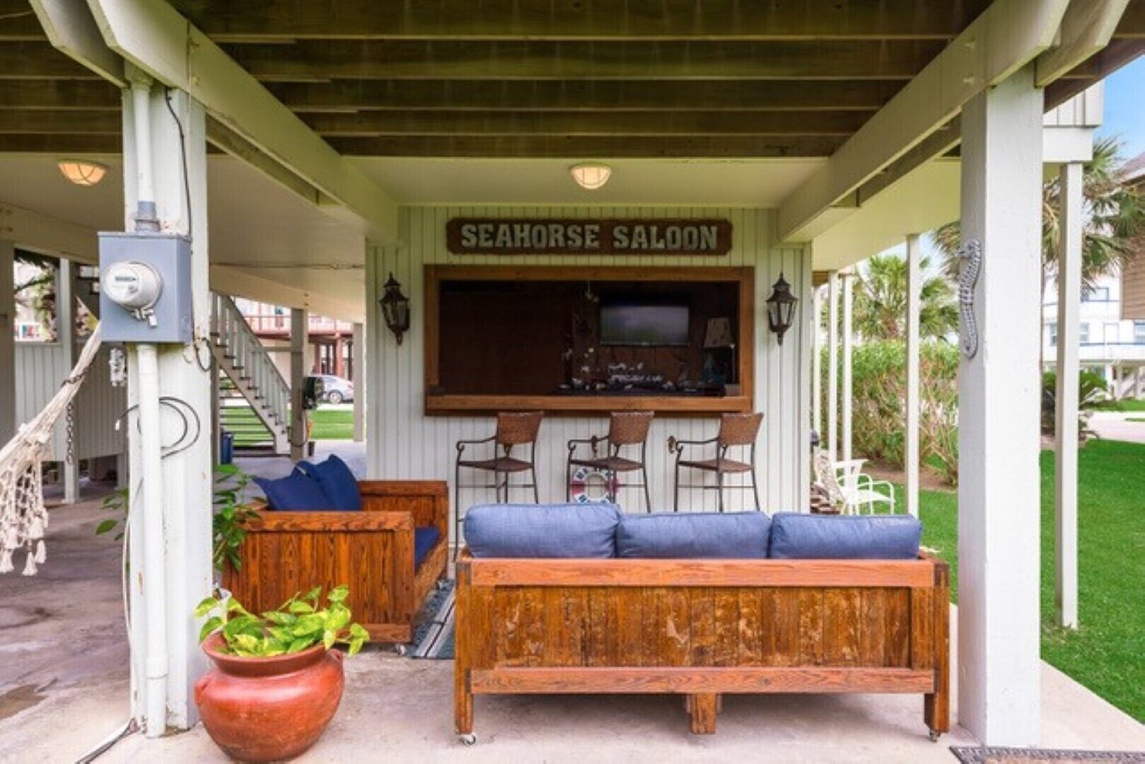 Ett takförsett utomhusområde med sittplatser, bestående av en träbänk och stolar, en bardisk och en skylt med texten "SEAHORSE SALOON".