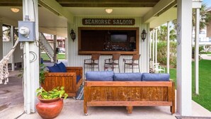 A covered outdoor seating area with a wooden bench and chairs, a bar counter, and a sign reading "SEAHORSE SALOON".