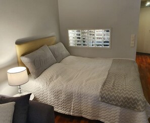 A neatly made bed with a quilted blanket, a headboard, and a window with a view of the outside.