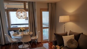Ett modernt vardagsrum med en matplats, en soffa, ett soffbord och utsikt över staden genom stora fönster.