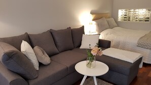 Ett modernt vardagsrum med en grå soffa, ett litet vitt sidobord och en vas med blommor.