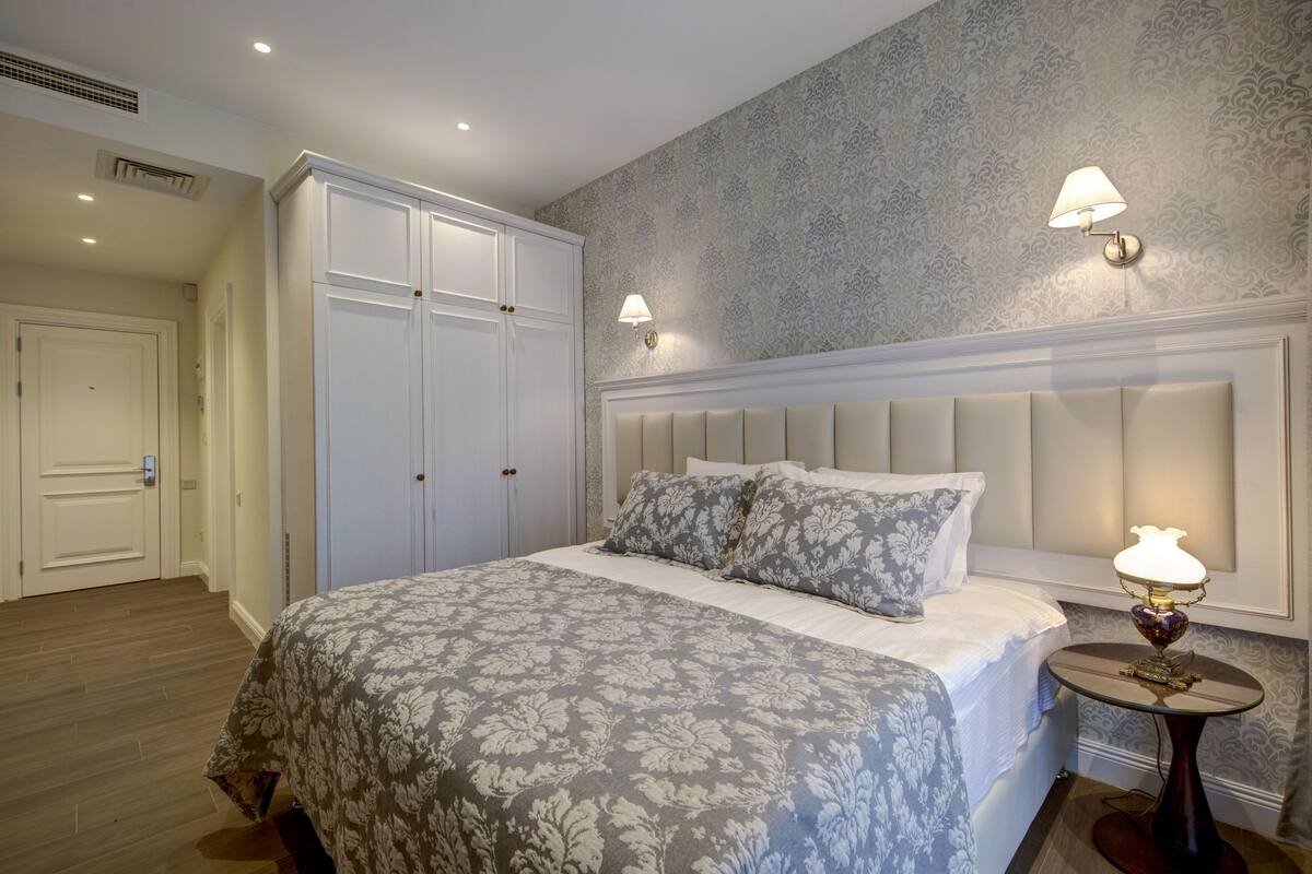 A bedroom with a large bed, a wardrobe, and two wall-mounted lamps.