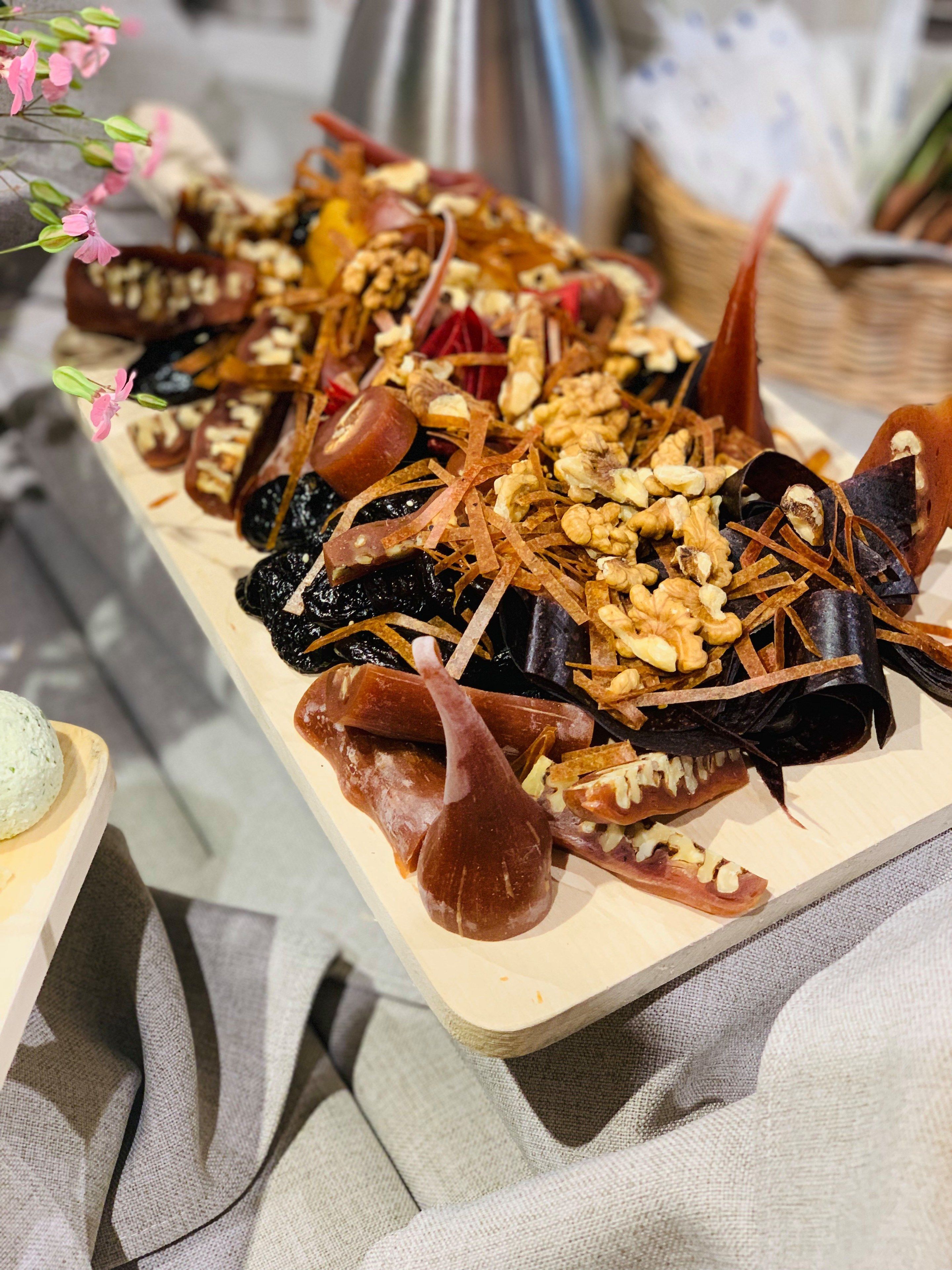 A wooden serving board with various food items including nuts, dried fruits, and possibly some meat.