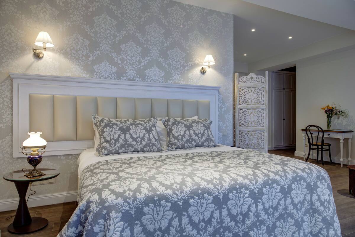 A bedroom with a large bed, two wall-mounted lamps, a small table with a lamp, and a decorative chair.