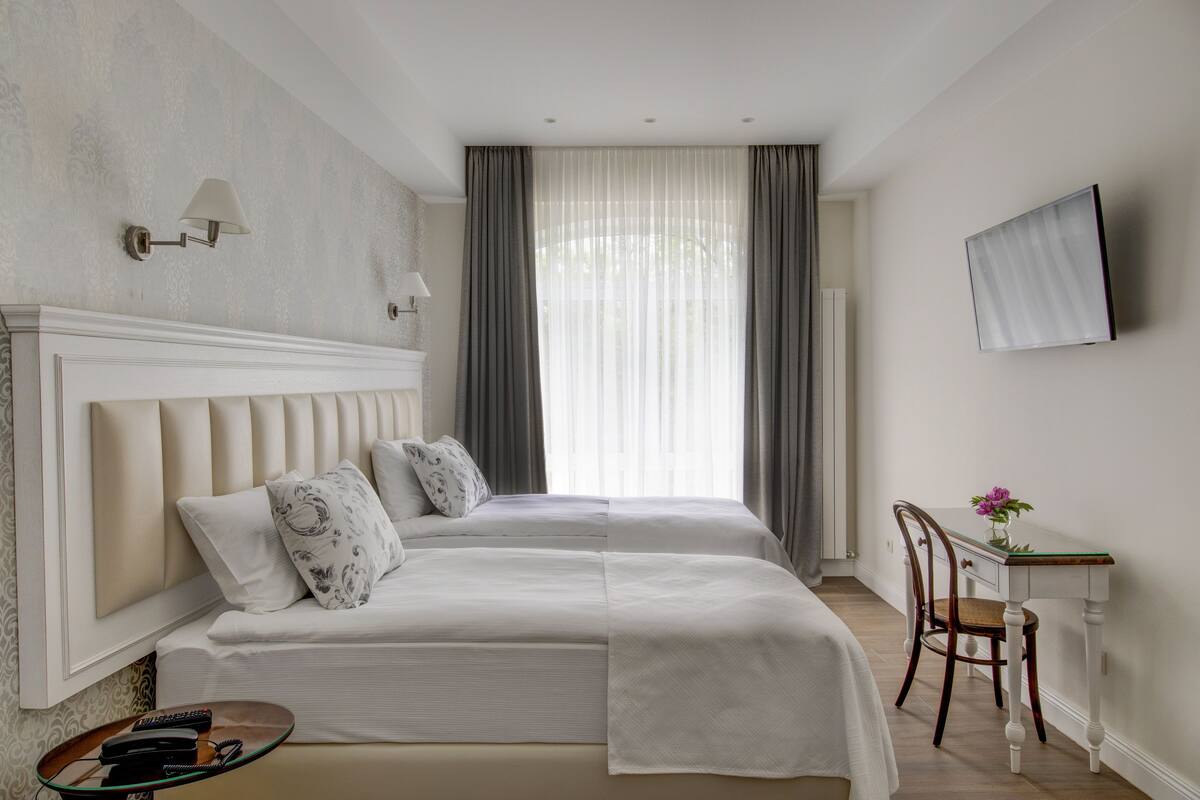 A hotel room with two beds, a desk, a chair, a TV, and a window with curtains.