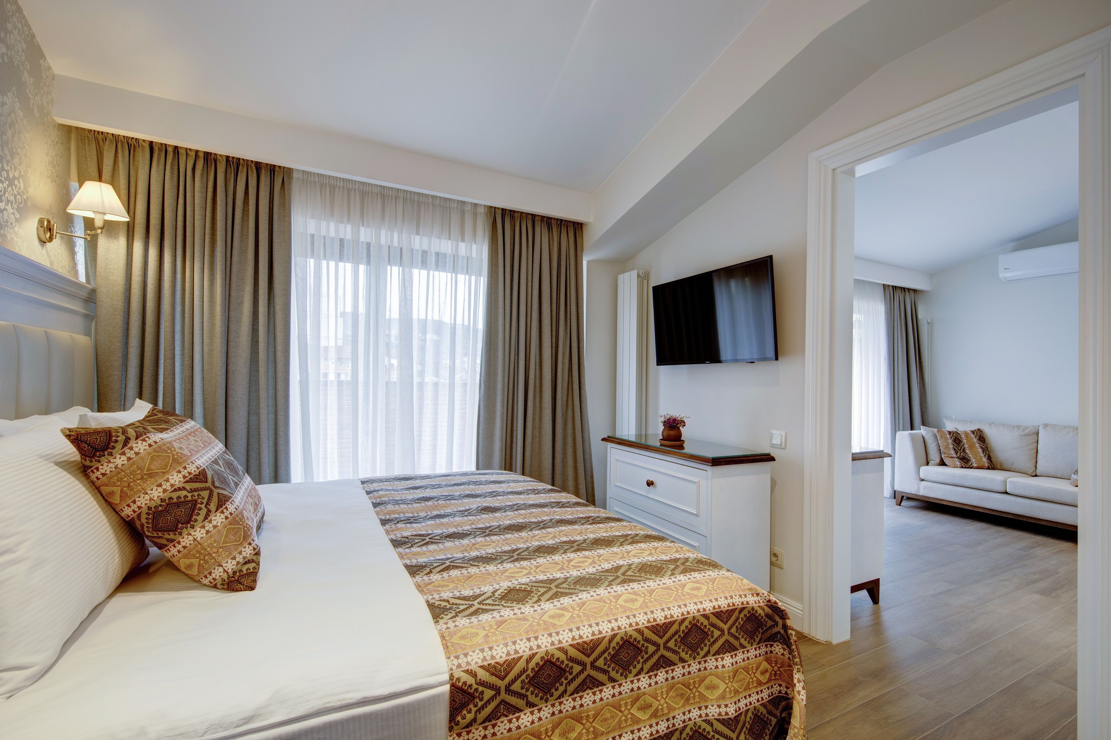 Ein Hotelzimmer mit Bett, Wandfernseher, Sofa und einem fenster mit Vorhängen.