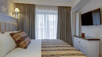 A hotel room with a large bed, a bedside table with a lamp, a TV mounted on the wall, and a window with curtains.