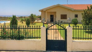 A two-story house with a red-tiled roof, a front gate, and a well-maintained lawn with a swimming pool in the background. - Cozy home in Maroni-Larnaca (Maroni-Larnaca)