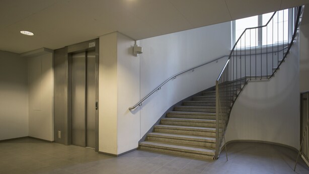A modern interior with a curved staircase, a pair of elevators, and a tiled floor. - 2ndhomes 2BR Penthouse with Balcony and Sauna (Helsinki)
