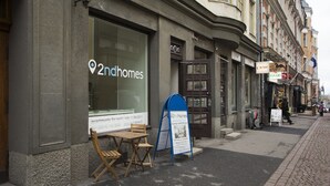 A 2ndhomes storefront with a large window, a small outdoor seating area, and a blue signboard. - 2ndhomes 2BR Penthouse with Balcony and Sauna (Helsinki)