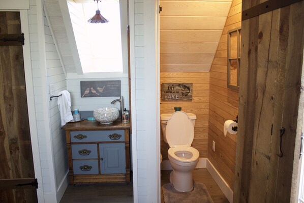 A rustic bathroom with a wooden vanity, a toilet, and a small window.