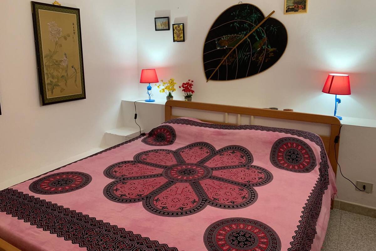 A bedroom with a bed, two bedside lamps, a wall-mounted decorative piece, and a framed artwork.