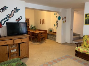 A living room with a television, wooden furniture, a dining area, and a staircase. - Le Residenze di Capo Falcone (Stintino)