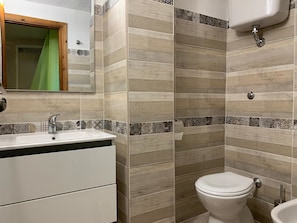 A bathroom with a sink, mirror, toilet, and a shower area. - Le Residenze di Capo Falcone (Stintino)