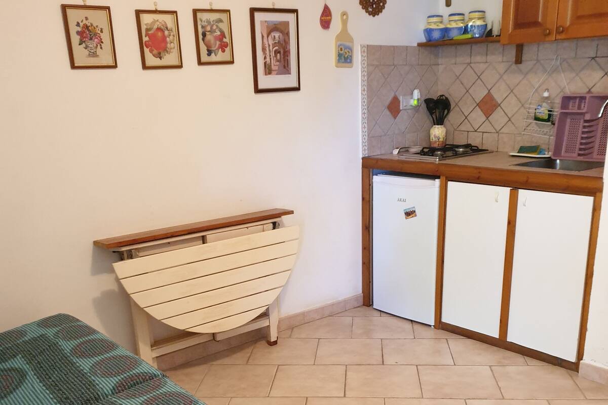 A small, cozy kitchen with a refrigerator, wooden cabinets, and a tiled backsplash.