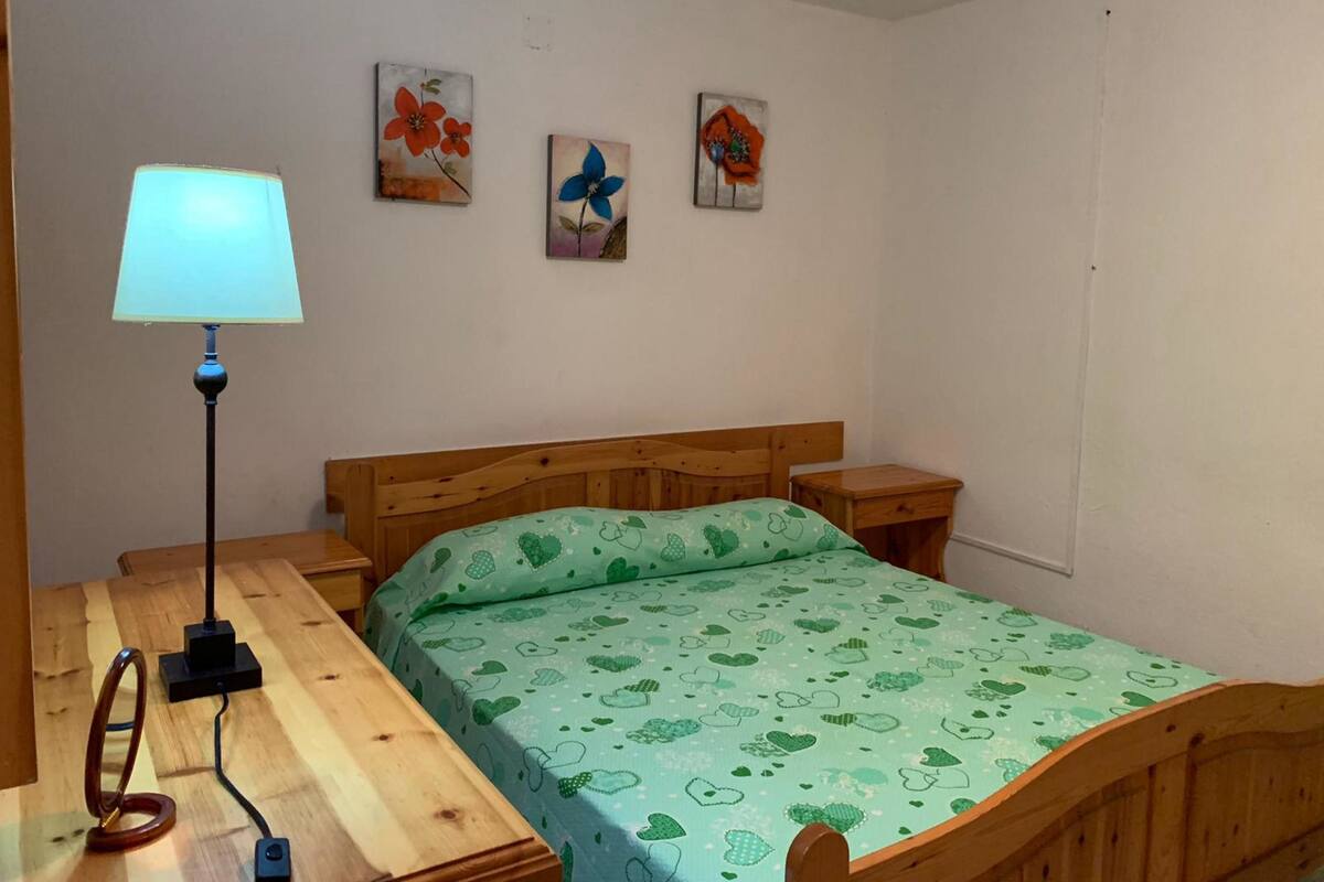 A bedroom with a wooden bed, a bedside table, a lamp, and three wall paintings.