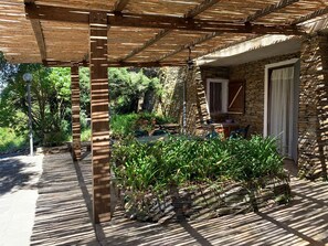 Un espacio al aire libre cubierto con un edificio de piedra, una pérgola de madera y plantas en macetas.