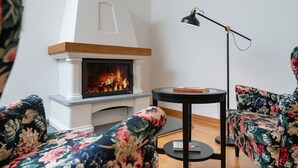 Un salón con chimenea, sofás de estampado floral, una mesa redonda negra y una lámpara de pie.