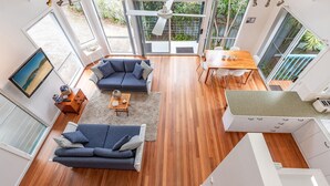 Ein geräumiges Wohnzimmer mit einem dunkelblauen Sofa, einem Holzesstisch und einer Küche mit weißer Arbeitsplatte.