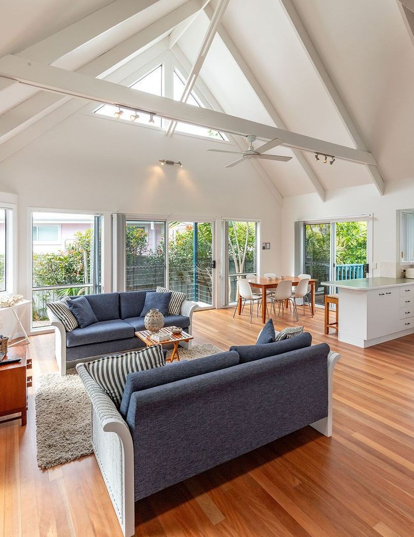 A spacious living area with a high ceiling, large windows, and a modern kitchen.