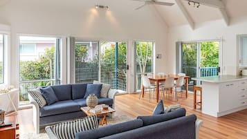A spacious living area with a high ceiling, large windows, and a kitchen area.
