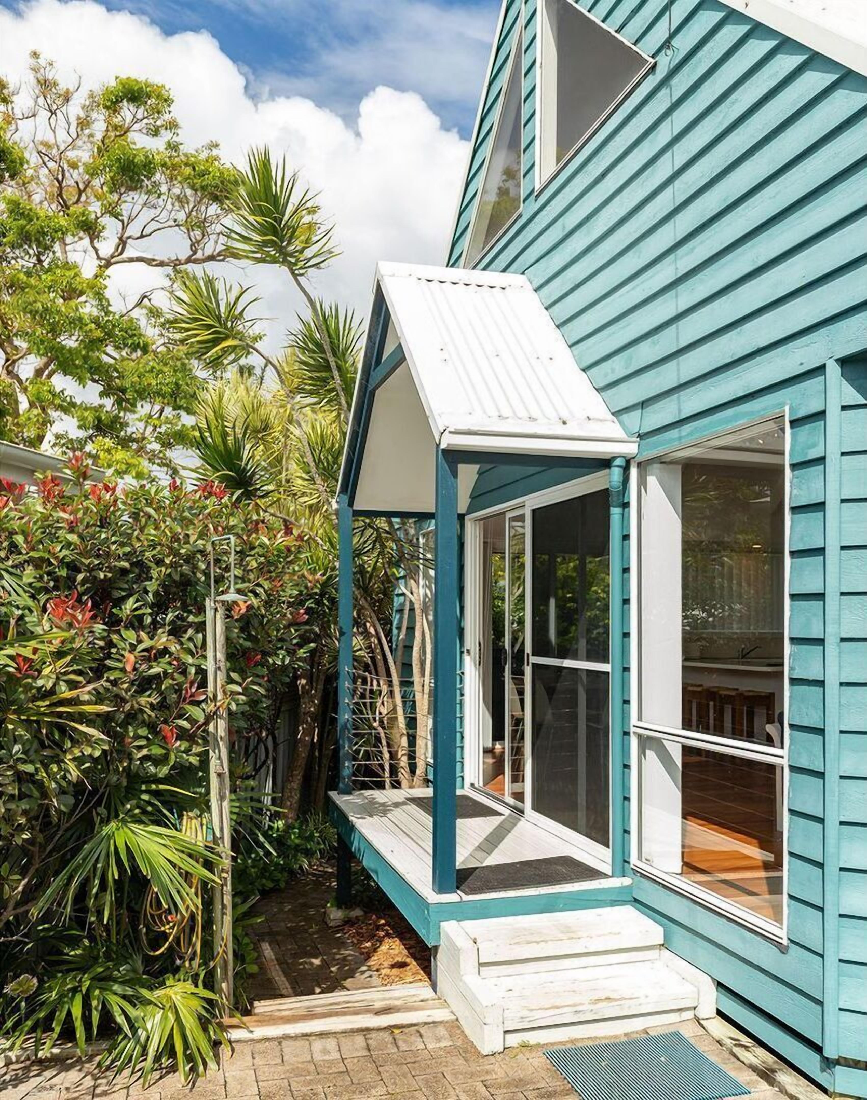 A modern house with a blue exterior, a covered porch, and a garden with various plants.