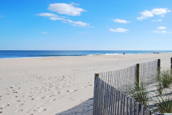Une plage avec une clôture en bois, des empreintes de pas et un ciel dégagé.