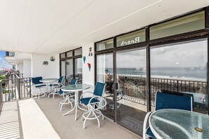 Une terrasse en bord de mer, dotée de sièges extérieurs et de grandes fenêtres donnant sur l’océan.