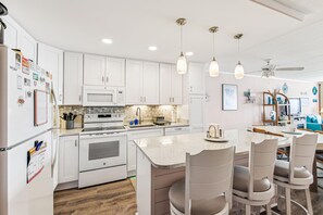 Una cocina moderna con armarios blancos, una isla central con asientos e iluminación colgante.