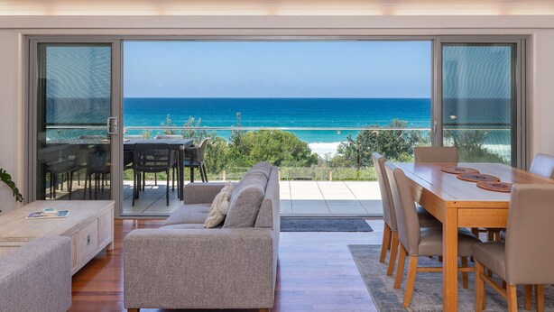 A modern living room with a large sliding glass door leading to a balcony overlooking the ocean.