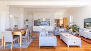 A modern living room with a dining area, a kitchen in the background, and a large window with a view.