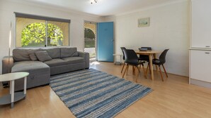 A compact living space with a grey sofa, a small round table with chairs, a blue door, and a white cabinet. - Bella Villa Manyana 19 great location short stroll to the beach and local shops (Blueys Beach)